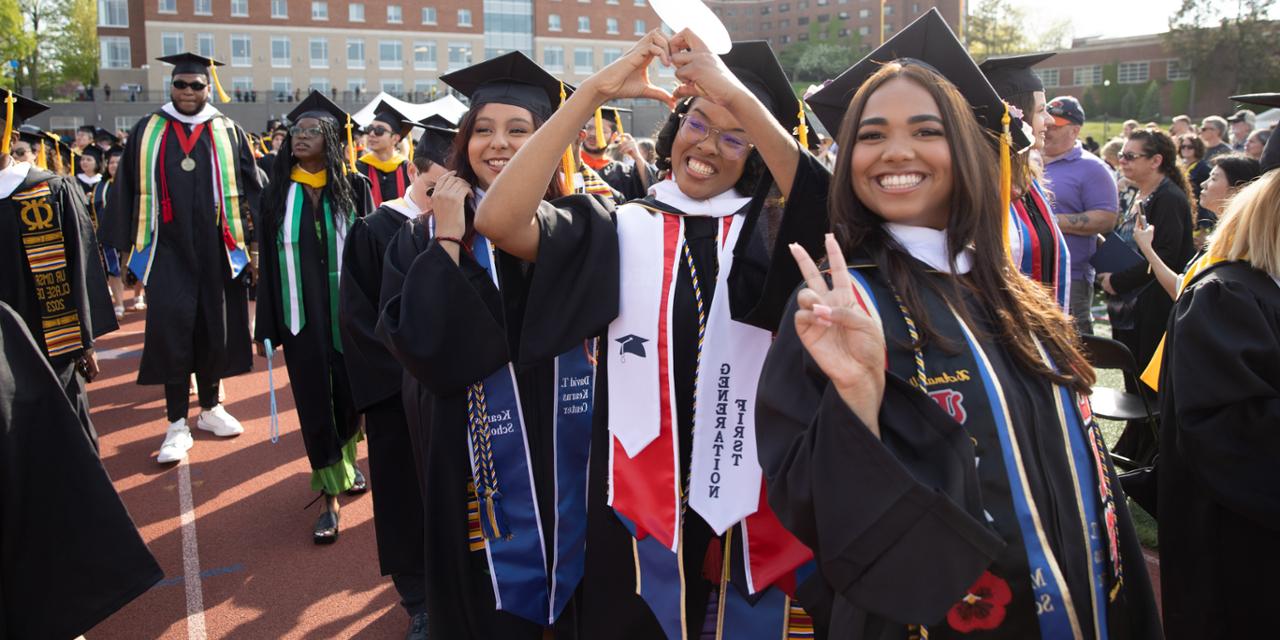 Students in caps and gowns smiling and posing at commencement